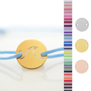 May include: A gold-colored bracelet with a wave design charm. The bracelet is made of a light blue cord and has a silver, gold, and rose gold charm option.