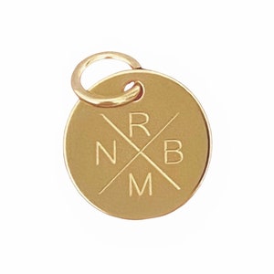 Puede incluir: Encanto ovalado de oro con un anillo para sujetarlo a un collar o pulsera. El encanto tiene un dise&ntilde;o grabado de cuatro letras, "N", "R", "B" y "M", dispuestas en forma de cruz.