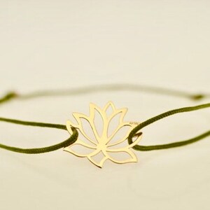 May include: A gold-colored lotus flower charm bracelet. The charm is a cutout design of the flower. The bracelet has a dark green cord. The bracelet is on a white background.