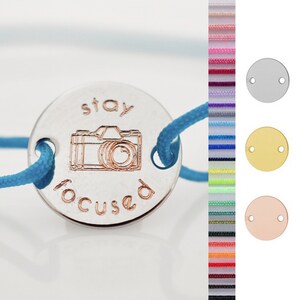 Peut inclure: Un bracelet à breloque argenté avec un cordon bleu. Le charme est rond et présente les mots "stay focused" et une icône d'appareil photo.