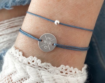 May include: Two blue cord bracelets with silver accents. One bracelet has a silver charm with the word "WIR" and an infinity symbol. The other bracelet has a single silver bead.