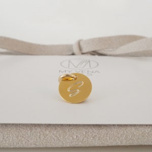May include: Gold charm with a cursive letter S engraved on a round disc. The charm has a ring attached to the top for attaching to a necklace or bracelet.