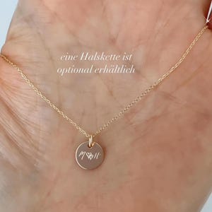 May include: A gold necklace with a small round pendant engraved with the word "MOM" and a heart. The text "eine Halskette ist optional erh&auml;ltlich" is visible in the image.