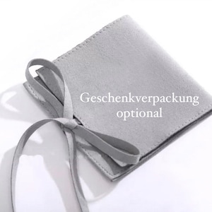 Op de afbeelding: Een grijze su&egrave;de tas met een trekkoord en de tekst "Geschenkverpackung optional" gedrukt op de voorkant.