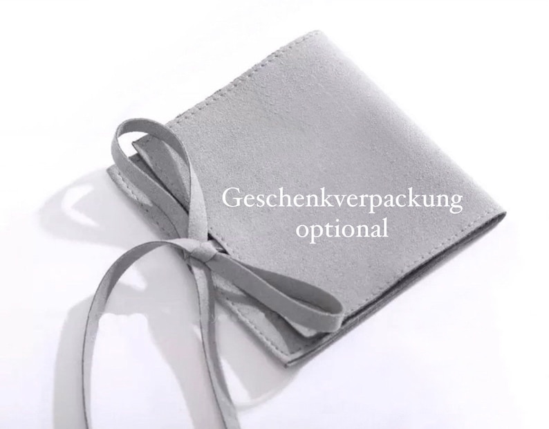Op de afbeelding: Een grijze su&egrave;de tas met een trekkoord en de tekst "Geschenkverpackung optional" gedrukt op de voorkant.