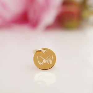 May include: Gold charm with a design of two hands holding pinky fingers together.