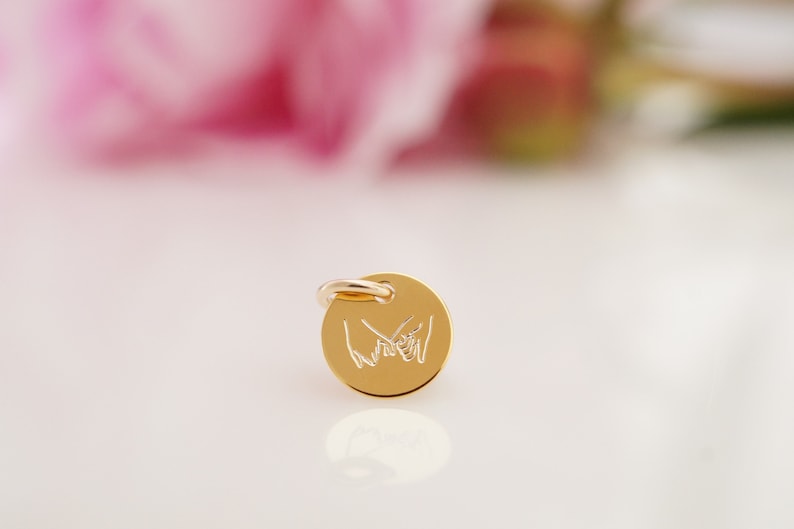 May include: Gold charm with a design of two hands holding pinky fingers together.