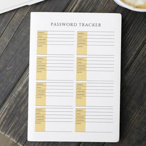 May include: A white Password Tracker notebook with a cream-colored vertical stripe on the right side of each page. The notebook is open, revealing lined sections for website, email, username, password, and notes. The title "PASSWORD TRACKER" is printed at the top.