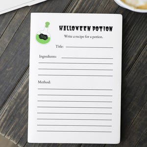 Pode incluir: Um caderno branco com tema de Halloween com as palavras "HALLOWEEN POTION" e "Write a recipe for a potion." impressas na capa. O caderno tem linhas para "Título", "Ingredientes" e "Método". Um gráfico de garrafa de poção verde também está na capa.