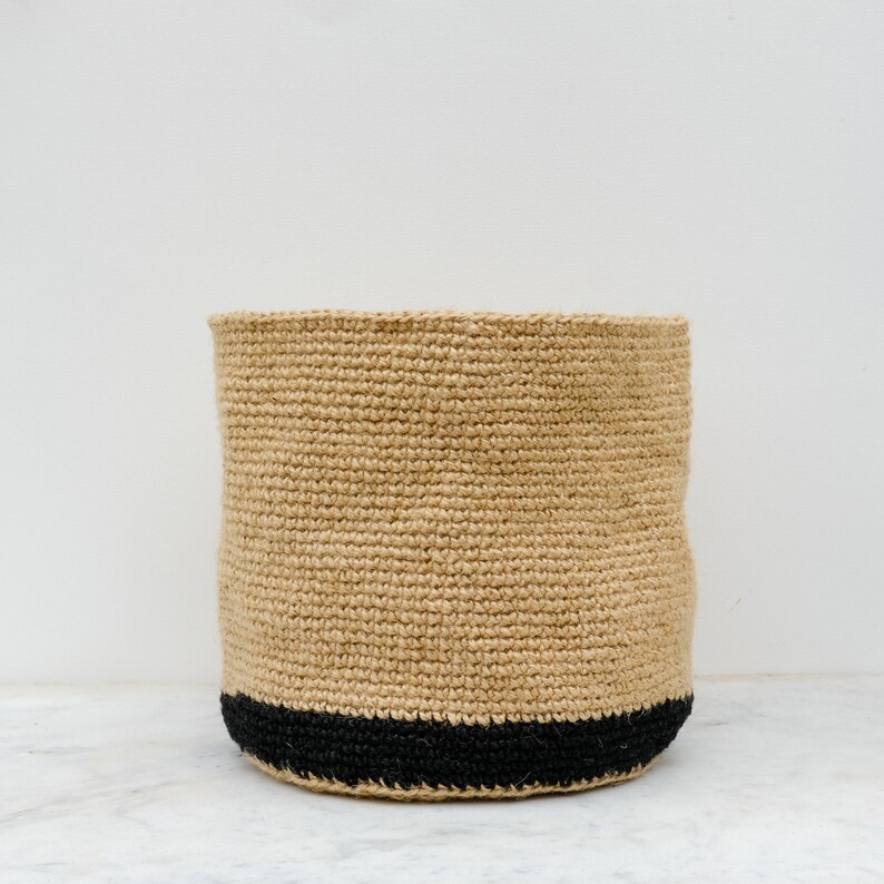May include: A natural woven storage basket with a black trim. The basket is made of a natural fiber and has a round shape.