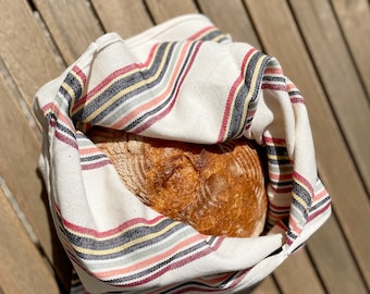 May include: A loaf of freshly baked bread wrapped in a striped kitchen towel with red, black, and yellow stripes.