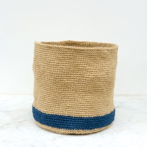 May include: A natural woven storage basket with a blue trim. The basket is made of a natural fiber and has a round shape.
