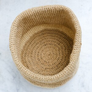 May include: A round, beige crocheted basket made of natural fibers. The basket has a textured, woven pattern and is perfect for storage or display.