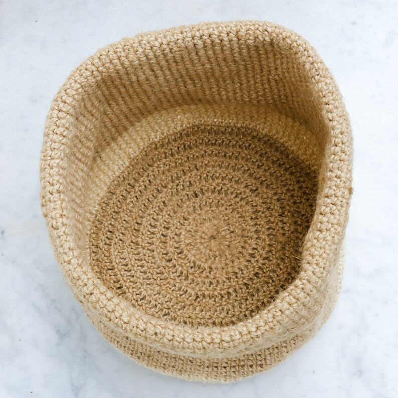 May include: A round, beige crocheted basket made of natural fibers. The basket has a textured, woven pattern and is perfect for storage or display.