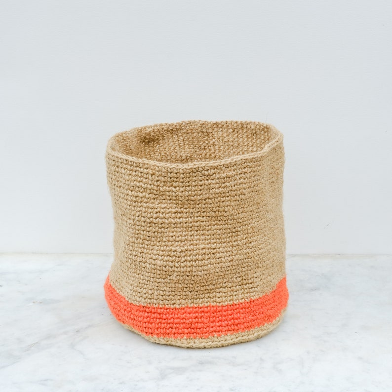 May include: A natural woven storage basket with a bright orange trim. The basket is made of a natural fiber and has a cylindrical shape.