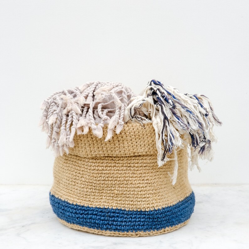 May include: A tan crocheted basket with a blue trim is filled with white and blue fringed fabric.