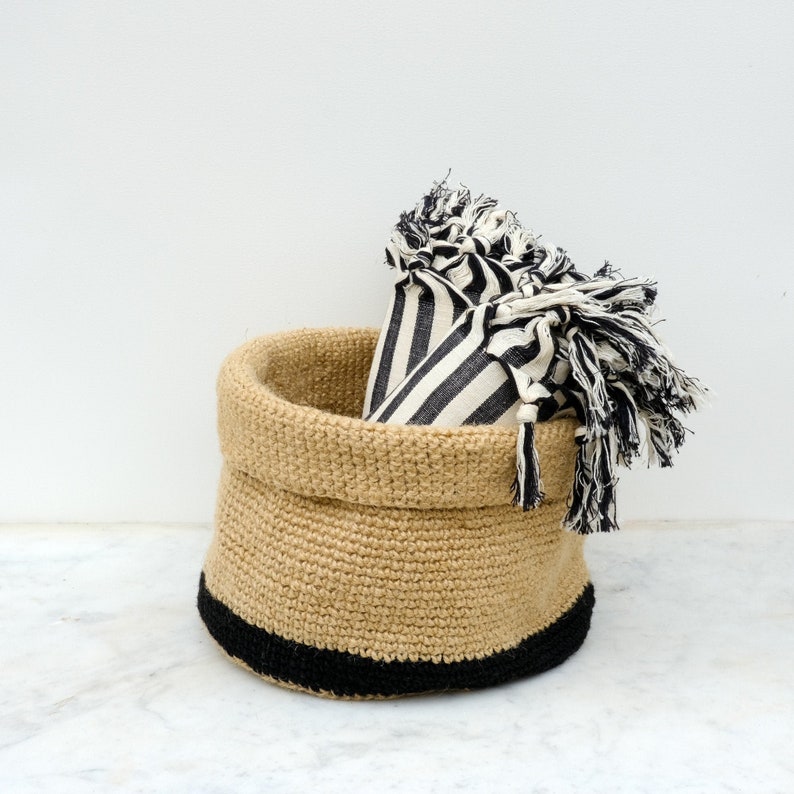 May include: A natural jute basket with a black trim, filled with black and white striped fabric.