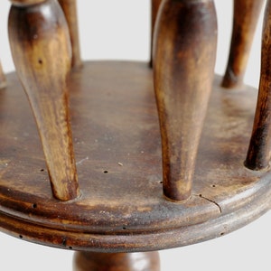 May include: A wooden stand with a round top and multiple spindles. The stand is made of dark brown wood and has a rustic appearance.