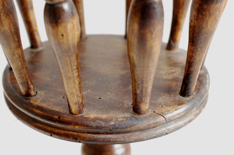 May include: A wooden stand with a round top and multiple spindles. The stand is made of dark brown wood and has a rustic appearance.