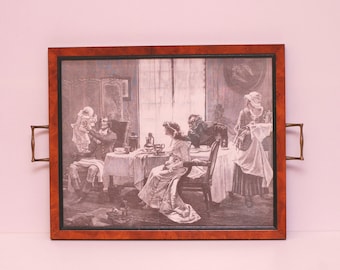 Puede incluir: Una bandeja de servir de madera vintage con asas de latón. La bandeja presenta una impresión en blanco y negro de una familia reunida alrededor de una mesa, con una mujer sirviendo té.