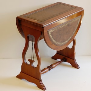 Op de afbeelding: Een houten klaptafel met een bruin leren blad. De tafel heeft een decoratief ontwerp op de poten en een gouden rand rond de rand van het blad.