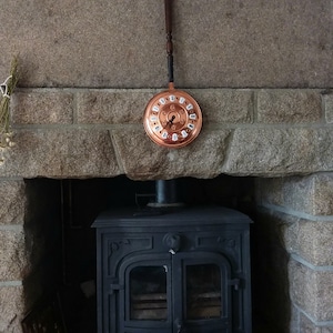 Peut inclure: Une horloge en cuivre suspendue au-dessus d'un poêle à bois noir dans une cheminée en pierre.