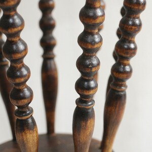 May include: A wooden stool with a round seat and five legs. The legs are turned and have a series of beads along their length. The stool is stained a dark brown color.