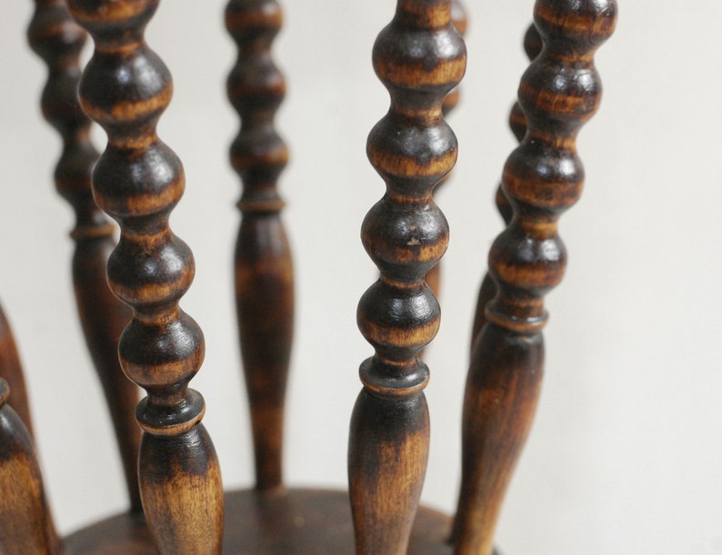 May include: A wooden stool with a round seat and five legs. The legs are turned and have a series of beads along their length. The stool is stained a dark brown color.