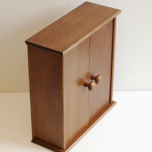 May include: A small wooden cabinet with two doors and two round wooden knobs. The cabinet is a dark brown color and has a smooth finish.