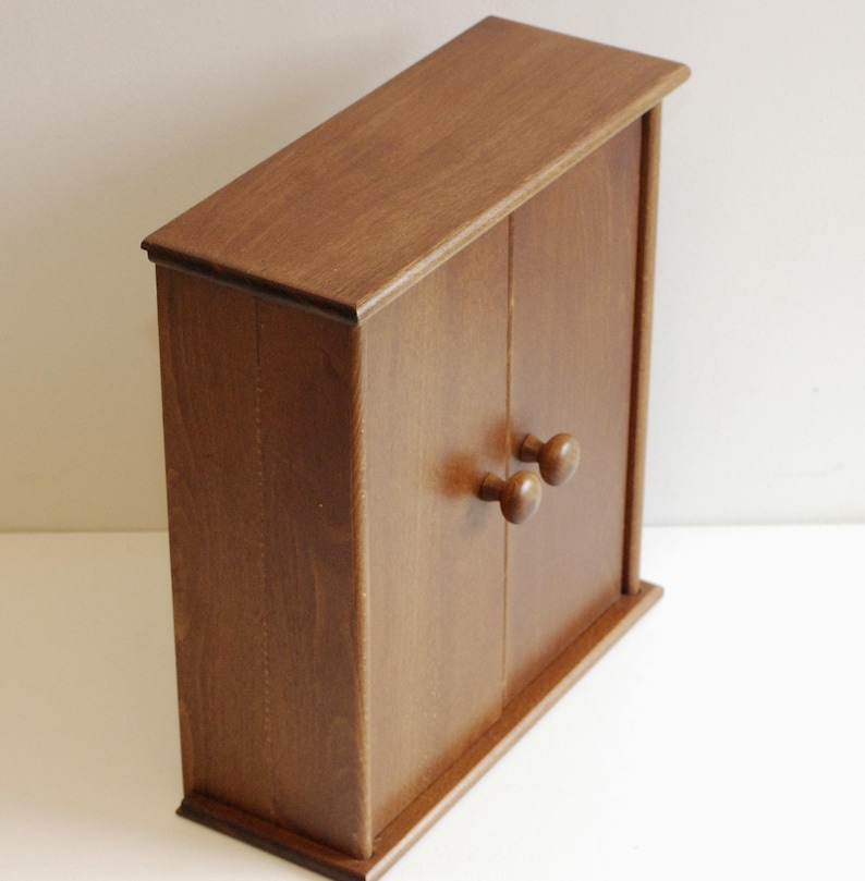 May include: A small wooden cabinet with two doors and two round wooden knobs. The cabinet is a dark brown color and has a smooth finish.
