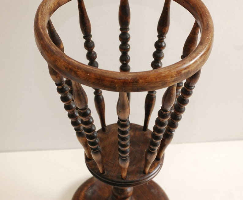 May include: A wooden plant stand with a round top and a base. The stand has a decorative design of small beads around the spindles.