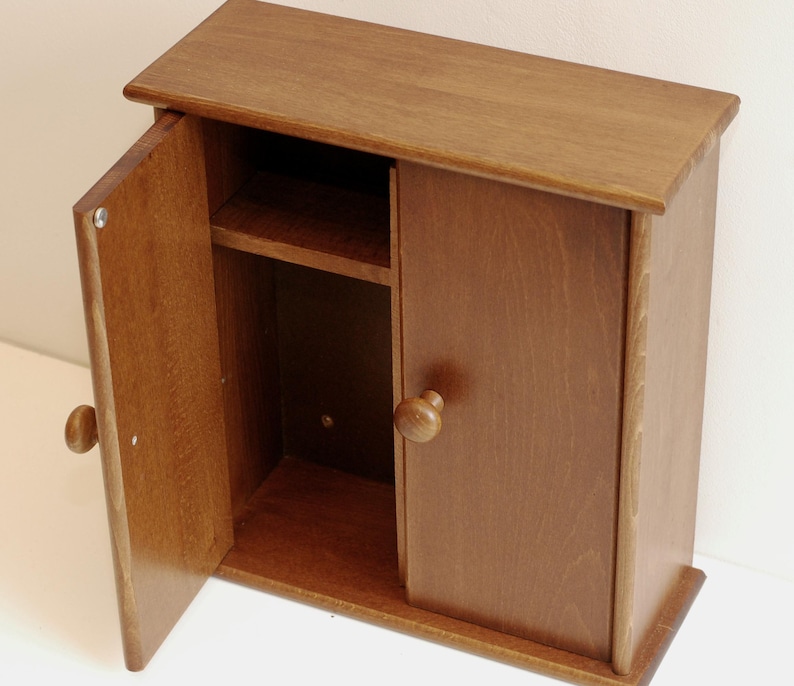 May include: A small wooden cabinet with a single door that is open. The cabinet has a shelf inside and a knob on the door. The cabinet is a light brown color.