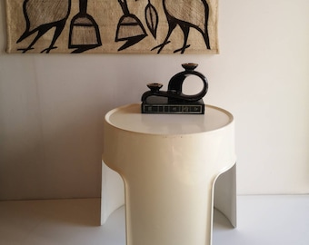 May include: A white, modern, sculptural side table with a round top and a unique, open, curved base. A black ceramic candle holder with three candle cups sits on the table.