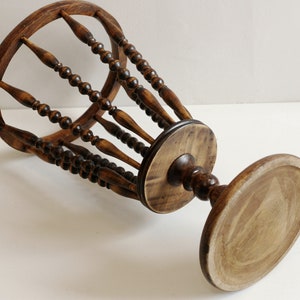 May include: A wooden umbrella stand with a round base and a cylindrical top. The top is made of a series of wooden spindles with beads.