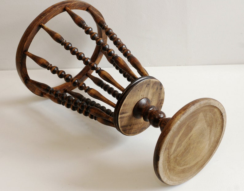 May include: A wooden umbrella stand with a round base and a cylindrical top. The top is made of a series of wooden spindles with beads.