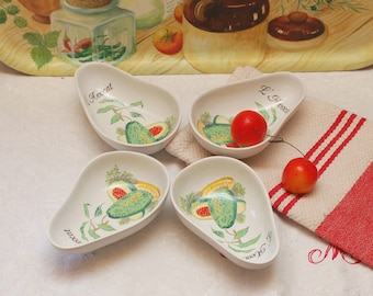 May include: Four white ceramic bowls shaped like avocado halves. Each bowl has a green avocado illustration and the text "L'avocat" in black script. The bowls are on a white tablecloth with a red and white striped towel.