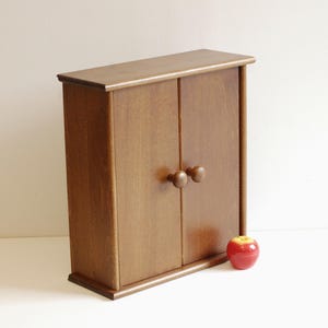 May include: A small wooden cabinet with two doors and round knobs. The cabinet is a light brown color and has a simple design.