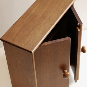 May include: A small wooden cabinet with two doors. The doors are open and the interior is visible. The cabinet is made of a light brown wood and has a simple design.