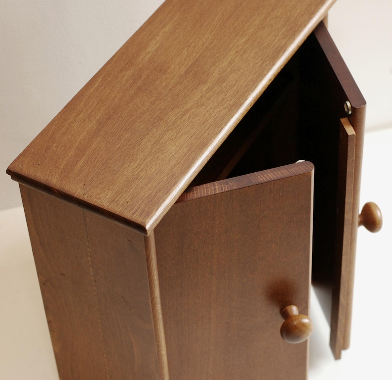 May include: A small wooden cabinet with two doors. The doors are open and the interior is visible. The cabinet is made of a light brown wood and has a simple design.