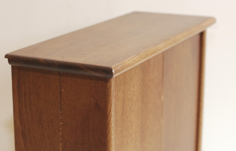 May include: A wooden cabinet with two doors. The cabinet is made of a dark wood with a natural finish. The doors are closed and have a simple design.
