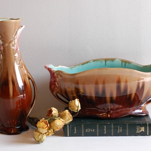 May include: A set of two vintage ceramic vases with a brown and teal glaze. The larger vase is oval shaped and has two handles. The smaller vase is tall and slender with a narrow neck. Both vases have a floral design.