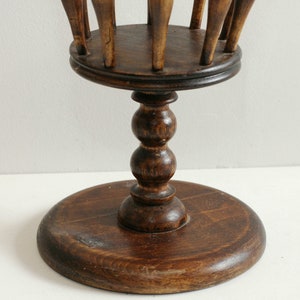 May include: A wooden stand with a round base and a pedestal with a decorative ball design. The top of the stand has a circular opening with wooden dowels sticking up.