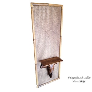 Puede incluir: Un panel de pared rectangular de bambú alto con un inserto de ratán tejido. El panel tiene un pequeño estante de madera y una cabeza de elefante de madera tallada montada en la pared.
