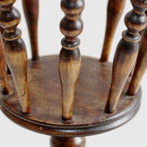 May include: A wooden plant stand with a round top and a single, round base. The stand has a decorative design with multiple spindles.