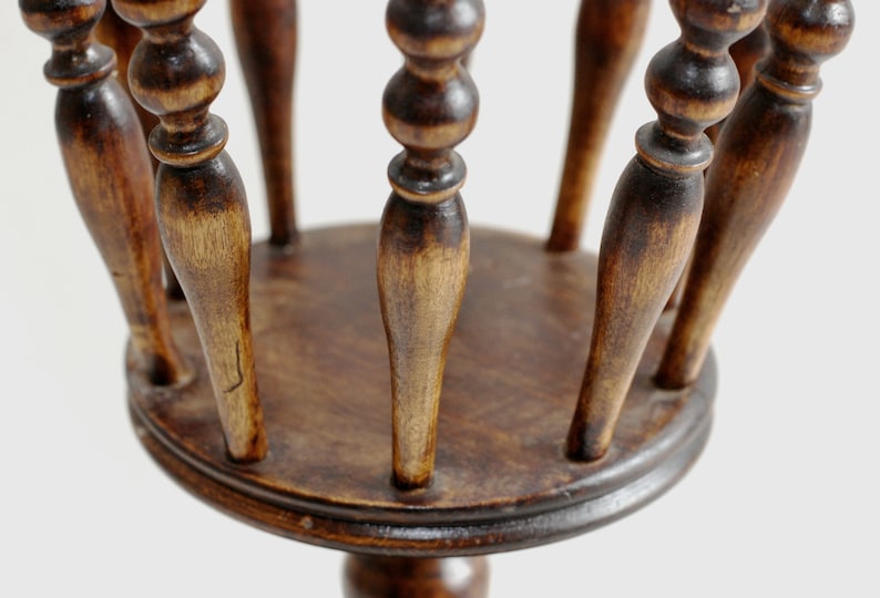 May include: A wooden plant stand with a round top and a single, round base. The stand has a decorative design with multiple spindles.