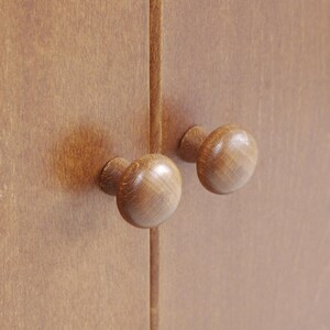 May include: Two wooden cabinet knobs with a rounded, mushroom-shaped design. The knobs are a light brown color and are mounted on a wooden cabinet door.