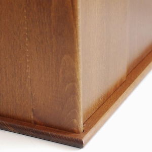 May include: A wooden box with a natural finish. The box has a hinged lid and a base with a slightly raised edge.