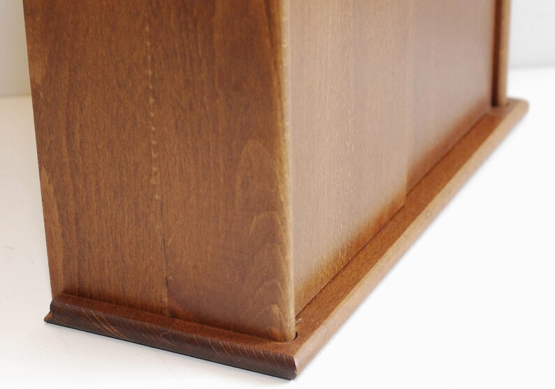 May include: A wooden box with a natural finish. The box has a hinged lid and a base with a slightly raised edge.