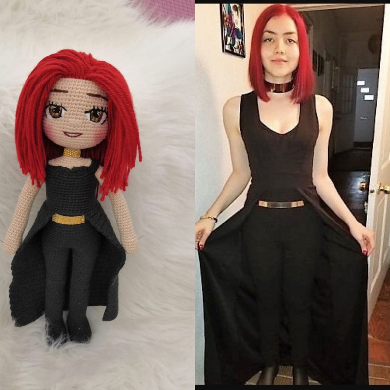 May include: A crocheted doll with red hair wearing a black dress with a gold belt. The doll is standing on a white surface.