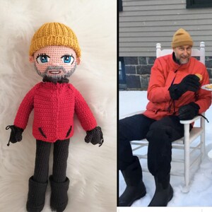 May include: A crocheted doll with a red jacket, black pants, and a yellow hat. The doll has a beard and a friendly expression. The doll is standing on a white fluffy surface.